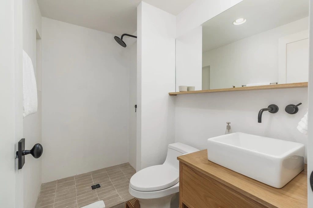 Clean white plaster bathroom with wood vanity, vessel sink and black fixtures