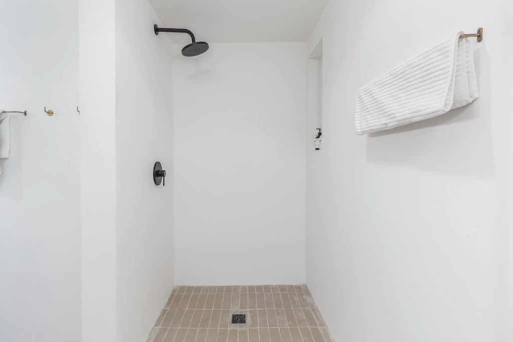 Smooth white plaster shower surround with black rain head and brass hooks