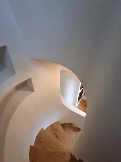 Curved smooth plaster stairwell with sculpted archway and warm wood treads