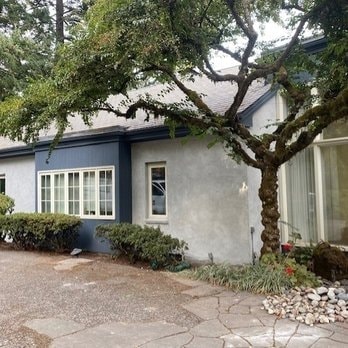 Blue-grey ranch home with stucco exterior and mature tree landscaping