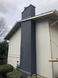Dark grey stucco chimney restoration on white siding home