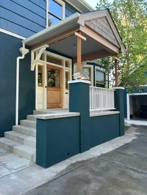 Teal craftsman home with stucco porch columns and wood door